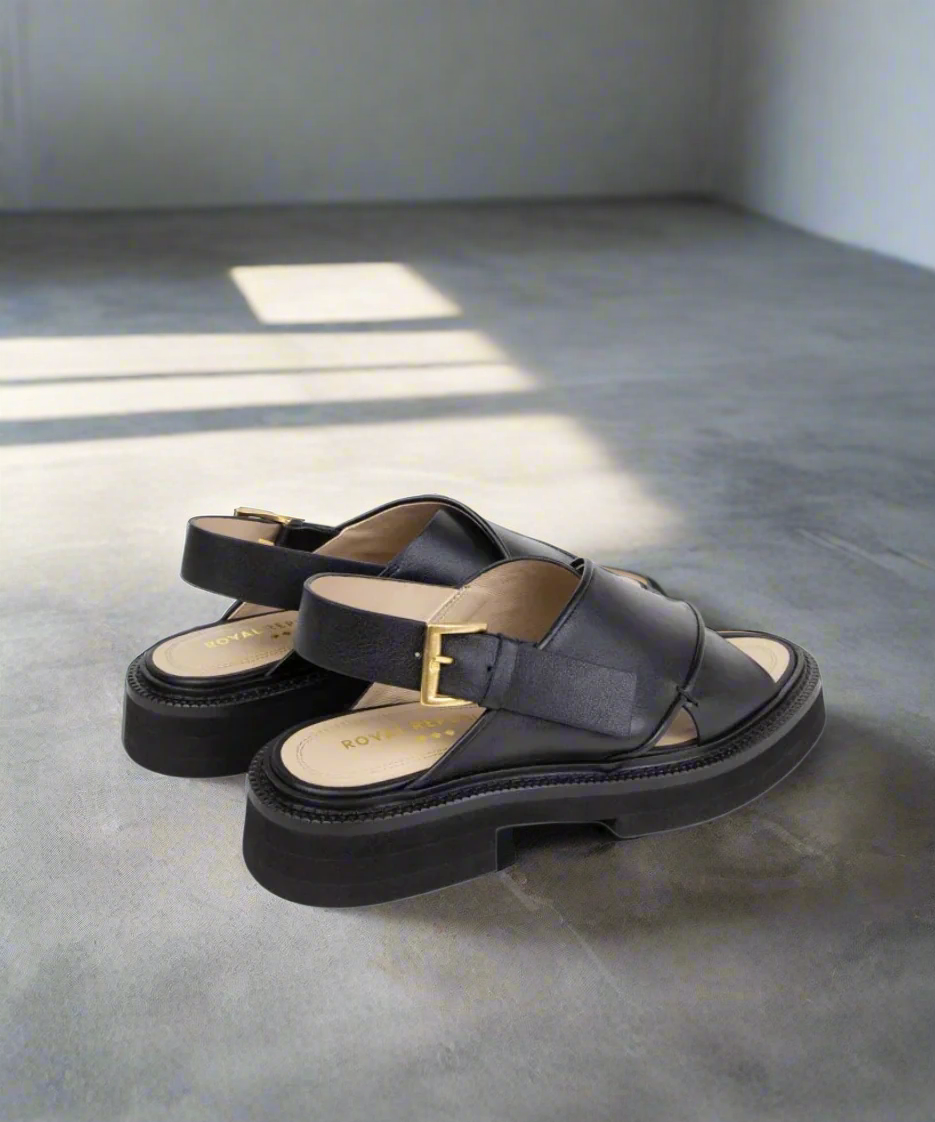 Black sandals with a gold buckle on a gray background