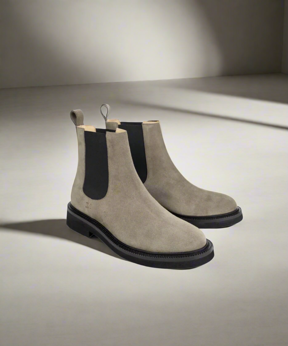 Pair of beige Chelsea boots with black soles on a white background