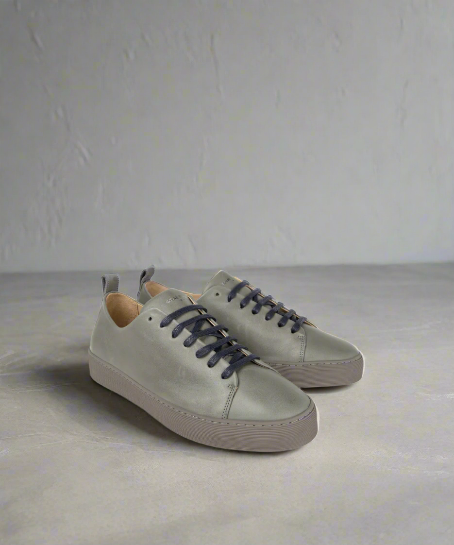 Pair of light gray sneakers with dark laces on a grey background