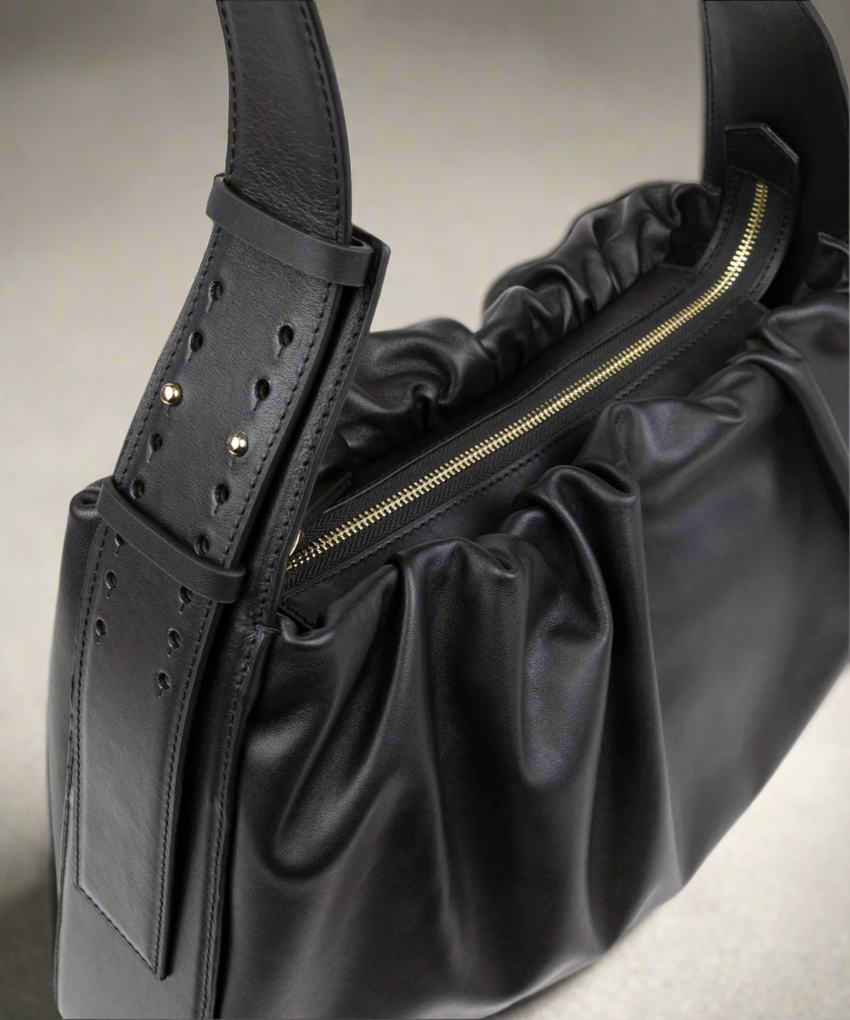 Black leather handbag with ruched design and gold zipper on a white background