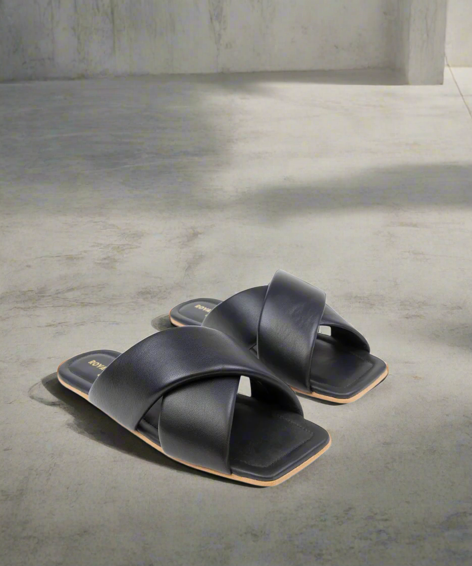 Black sandals with criss-cross straps on a grey background