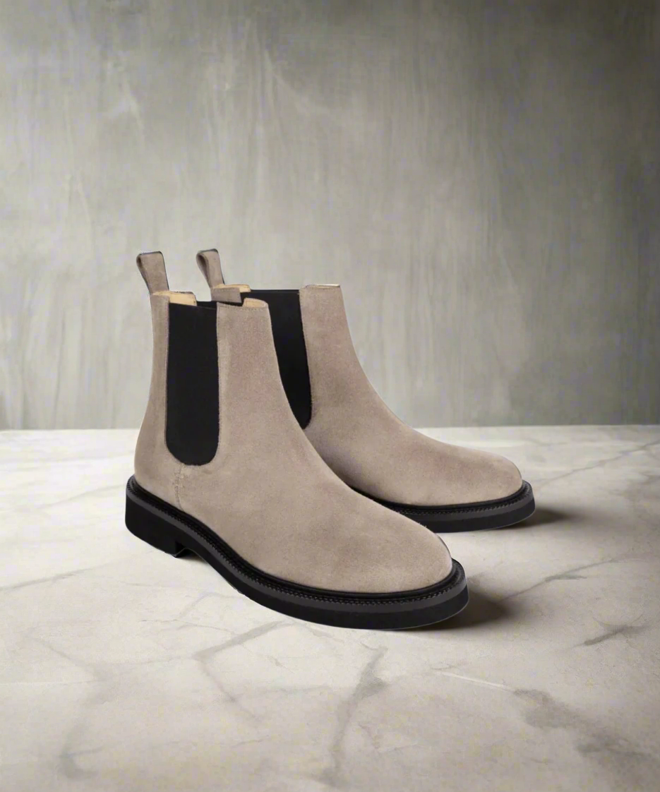 Pair of beige Chelsea boots with black soles on a gray background
