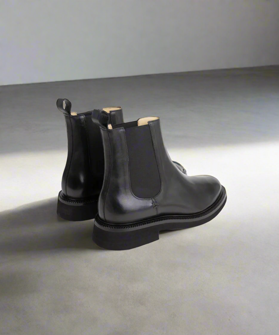 Pair of black leather Chelsea boots on a gray surface with a neutral background