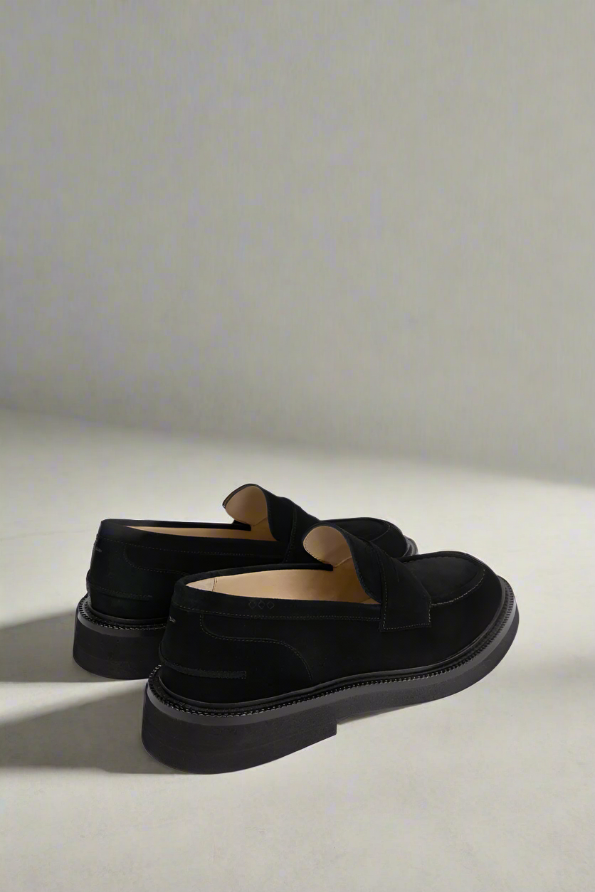 Pair of black Royal RepubliQ loafers on a light gray background