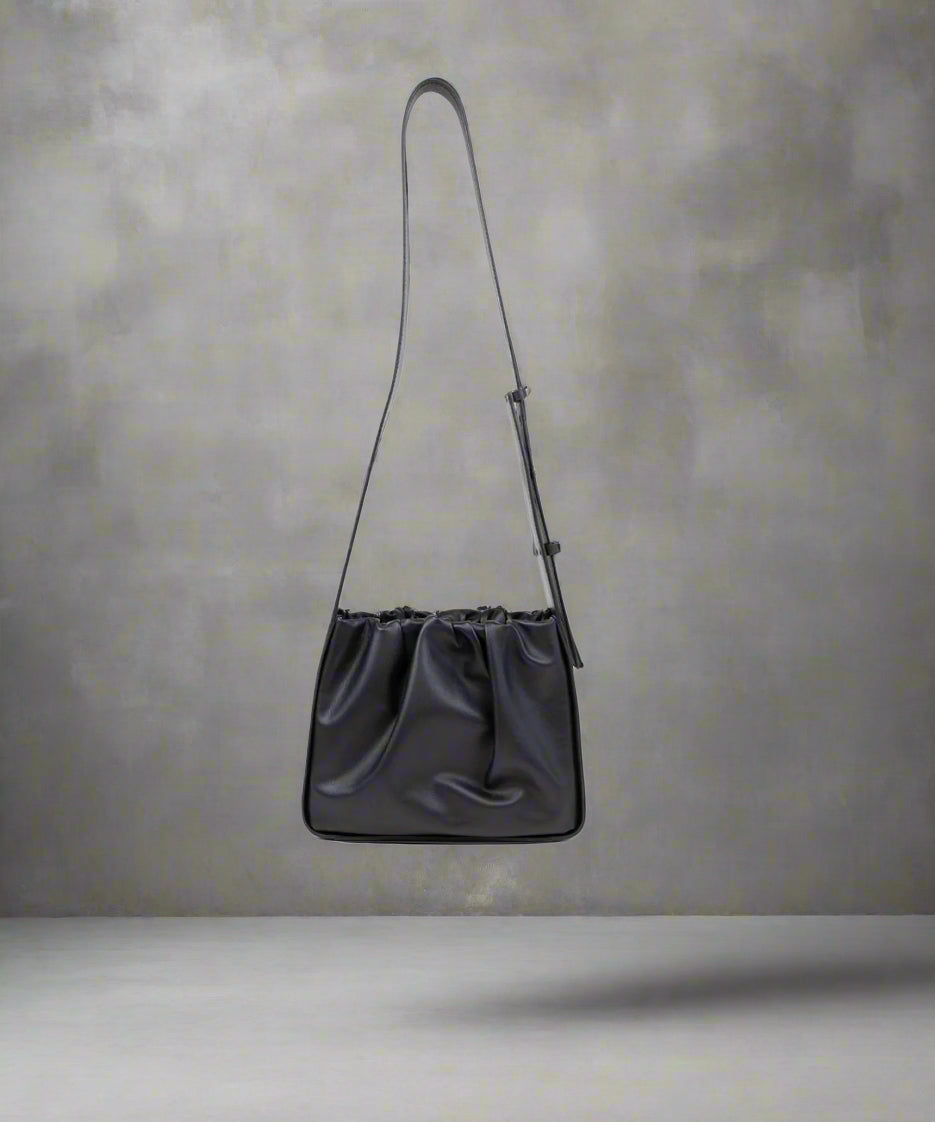 A black crossbody bag with a soft rectangular body and a protective stiff structure, featuring a shoulder strap and matt gold trimmings.