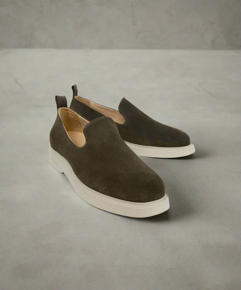 Pair of brown slip-on shoes with white soles on a gray background