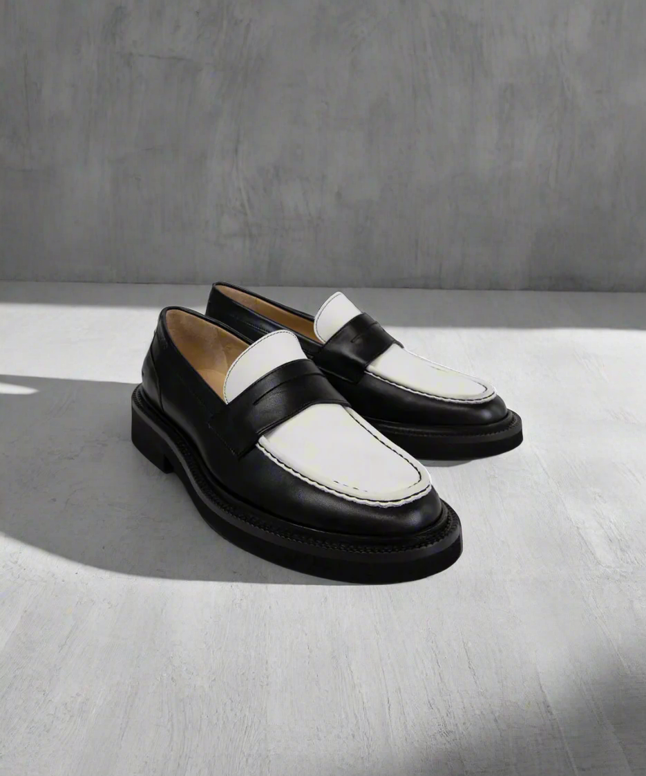 Black and white Royal RepubliQ loafers on a gray background