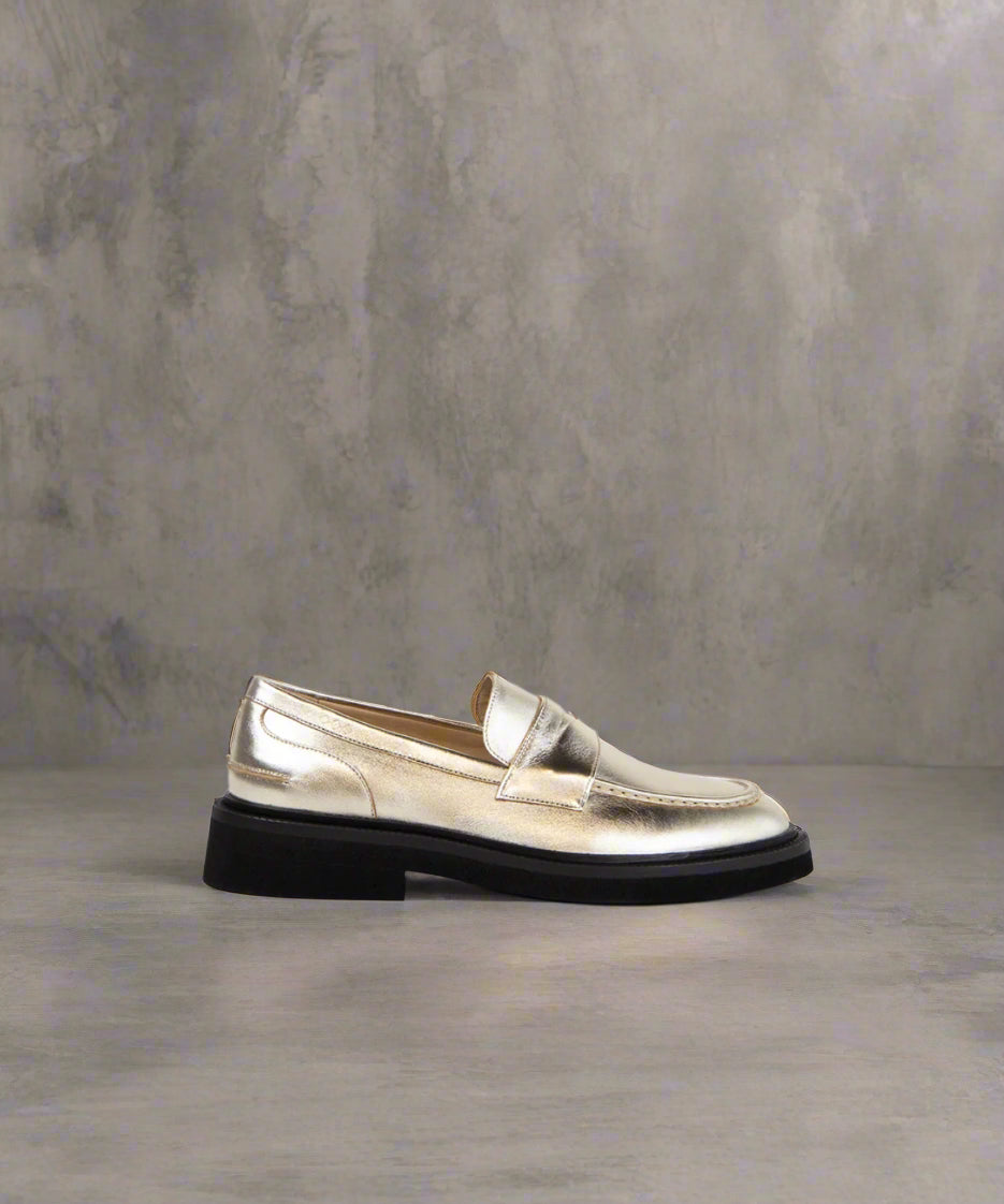 A single gold metallic loafer shoe with a flat sole and closed toe.