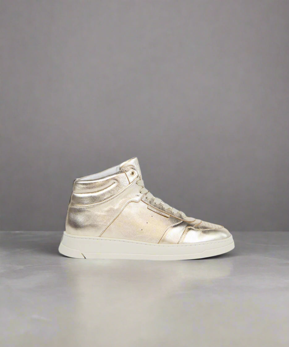 A metallic gold high-top sneaker with laces and a rubber sole on a gray background.