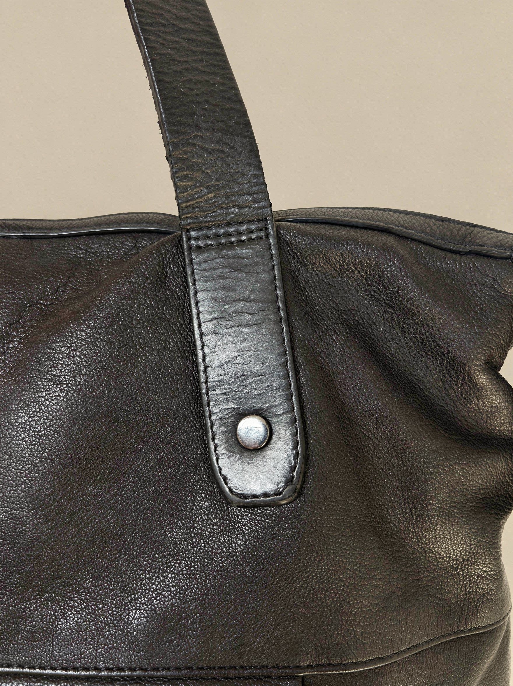 Close-up of a black leather bag with a strap and metal buckle on a beige background