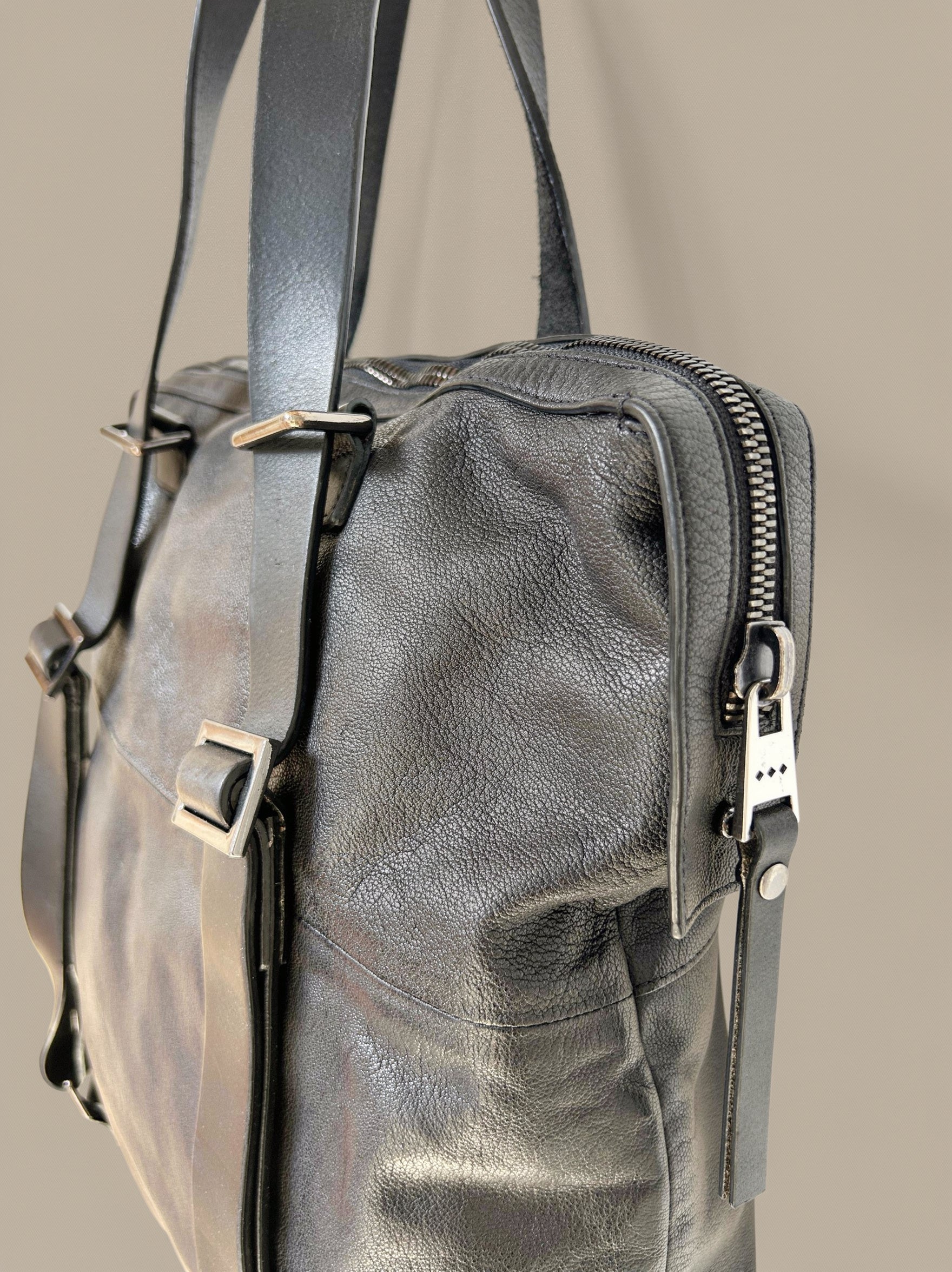 Black leather bag with zippers and straps on a beige background