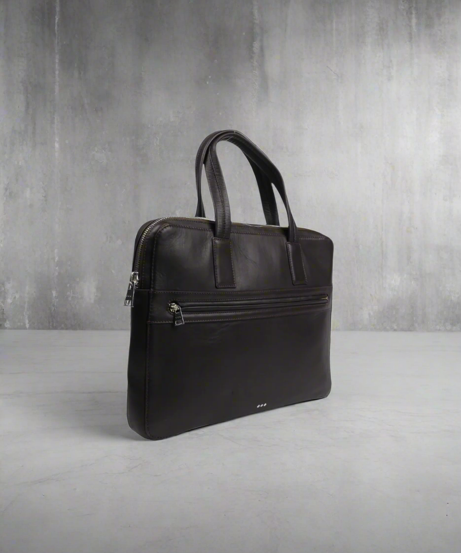 Brown Royal RepubliQ leather briefcase on a gray surface with a gray background