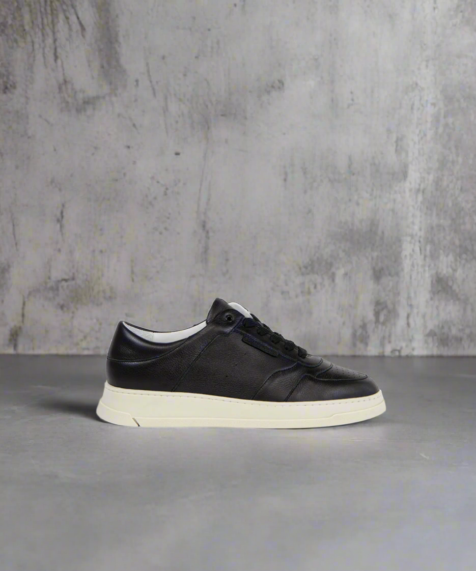 Black sneaker with white sole on a gray surface and concrete wall background