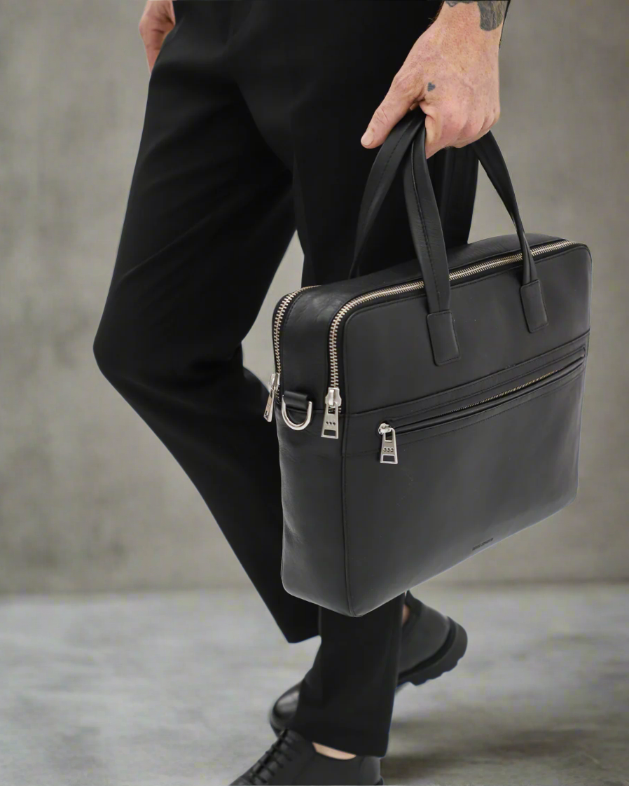 Person holding a black Royal RepubliQ leather briefcase against a gray background