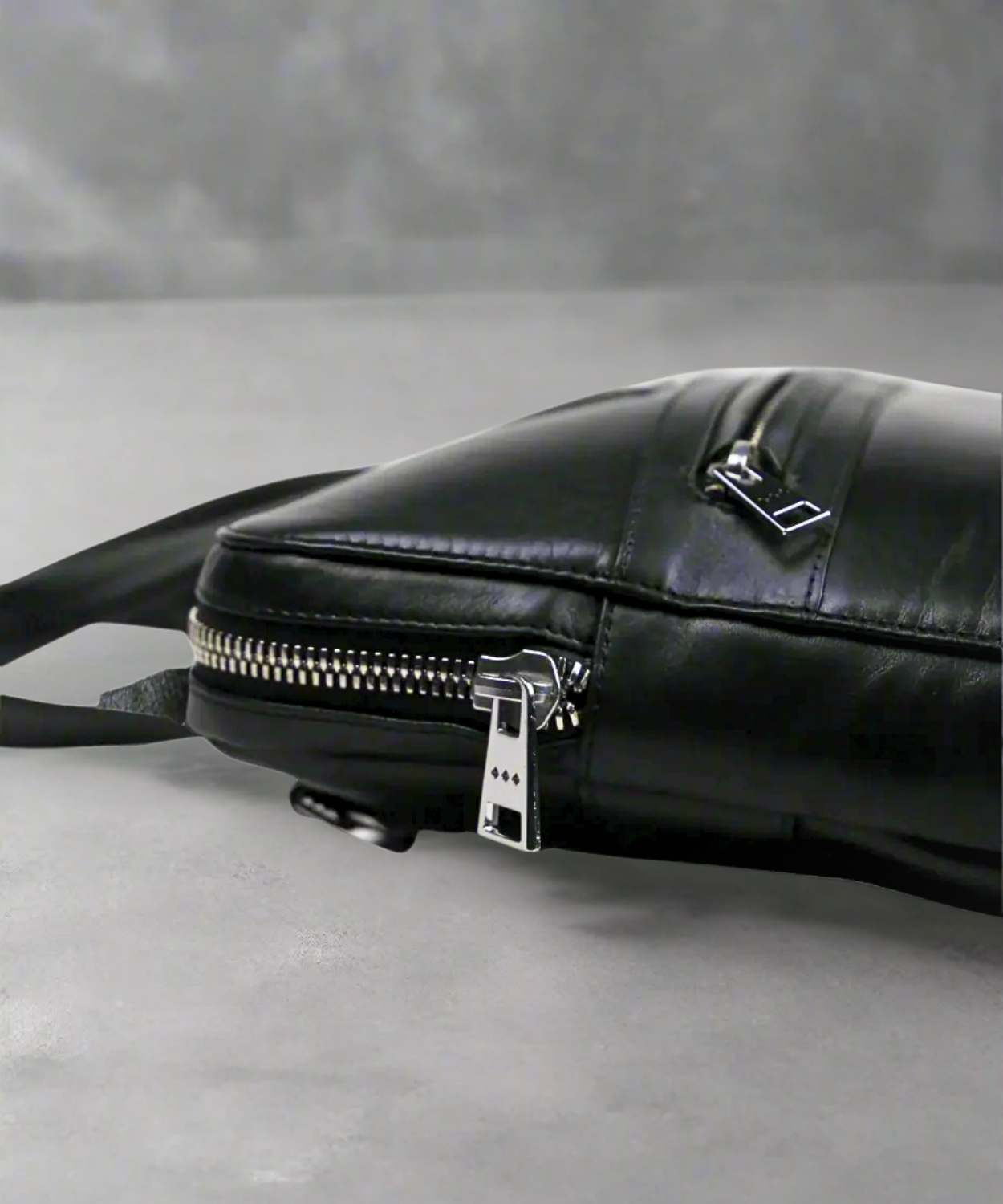 Black Royal RepubliQ leather bag with a zipper on a gray background