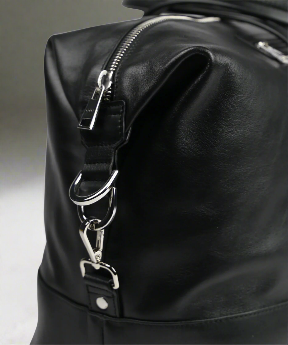 Close-up of a black Royal RepubliQ leather bag with silver zippers on a gray background