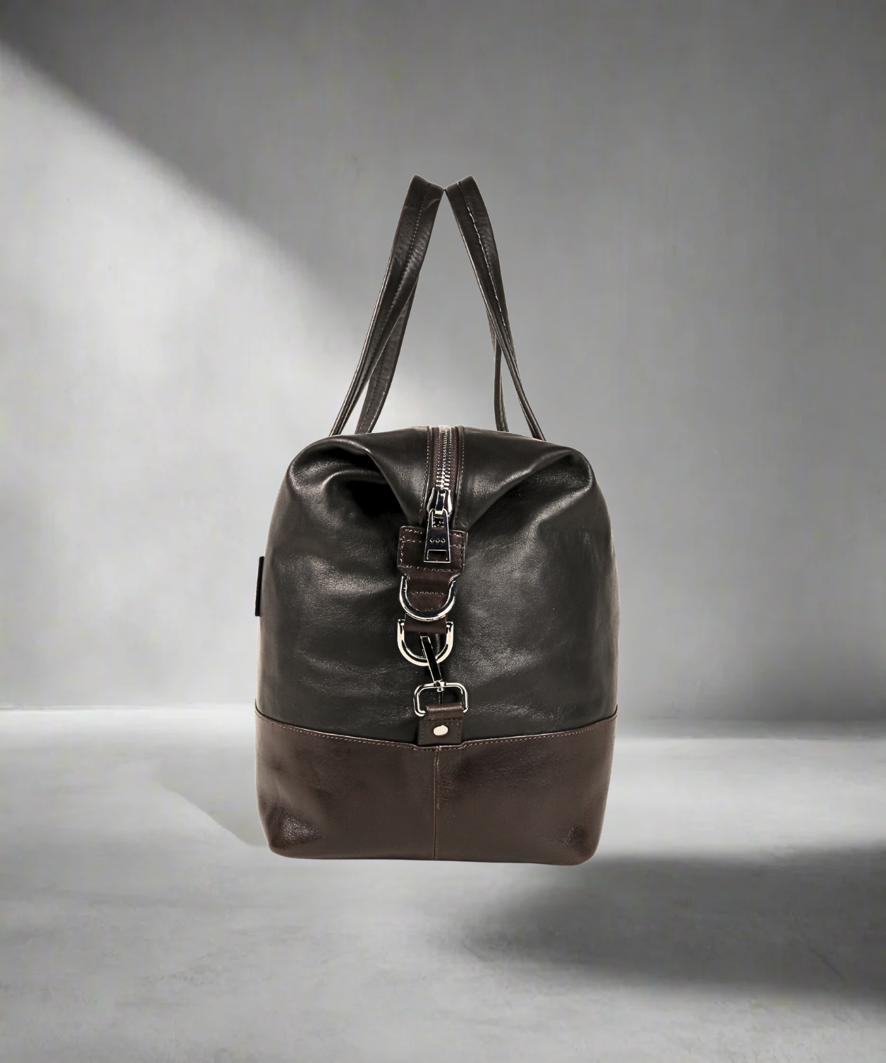 Brown Royal RepubliQ leather duffel bag with silver buckles on a gray background