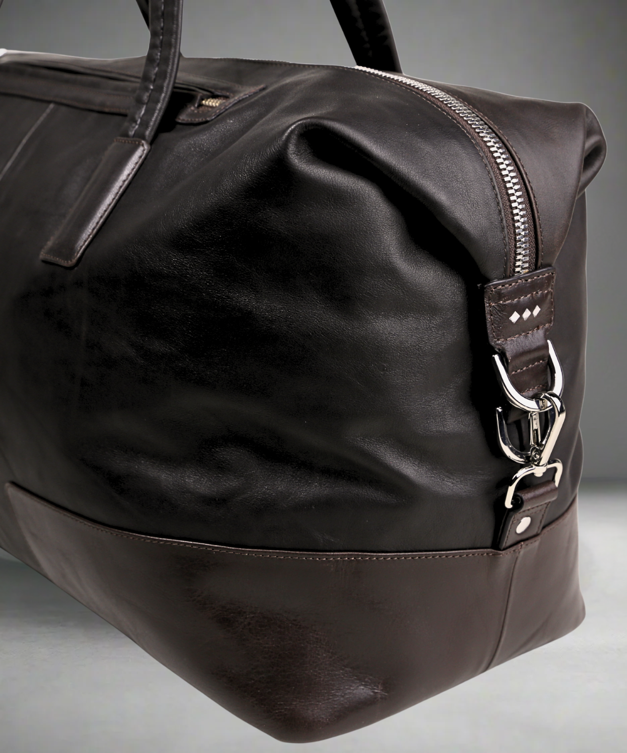 Brown Royal RepubliQ leather duffel bag with silver zipper and hardware on a gray background