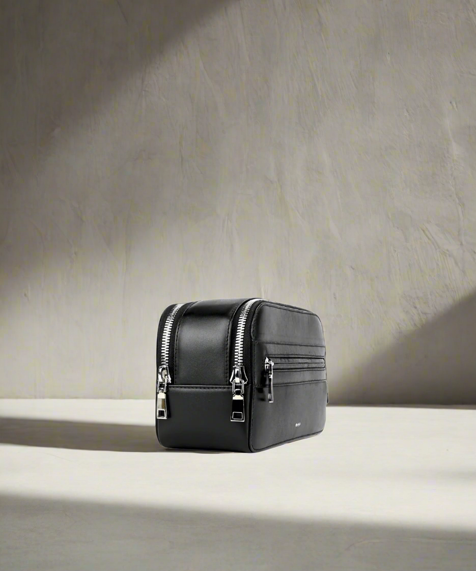 Black toiletry bag with silver zippers on a white background
