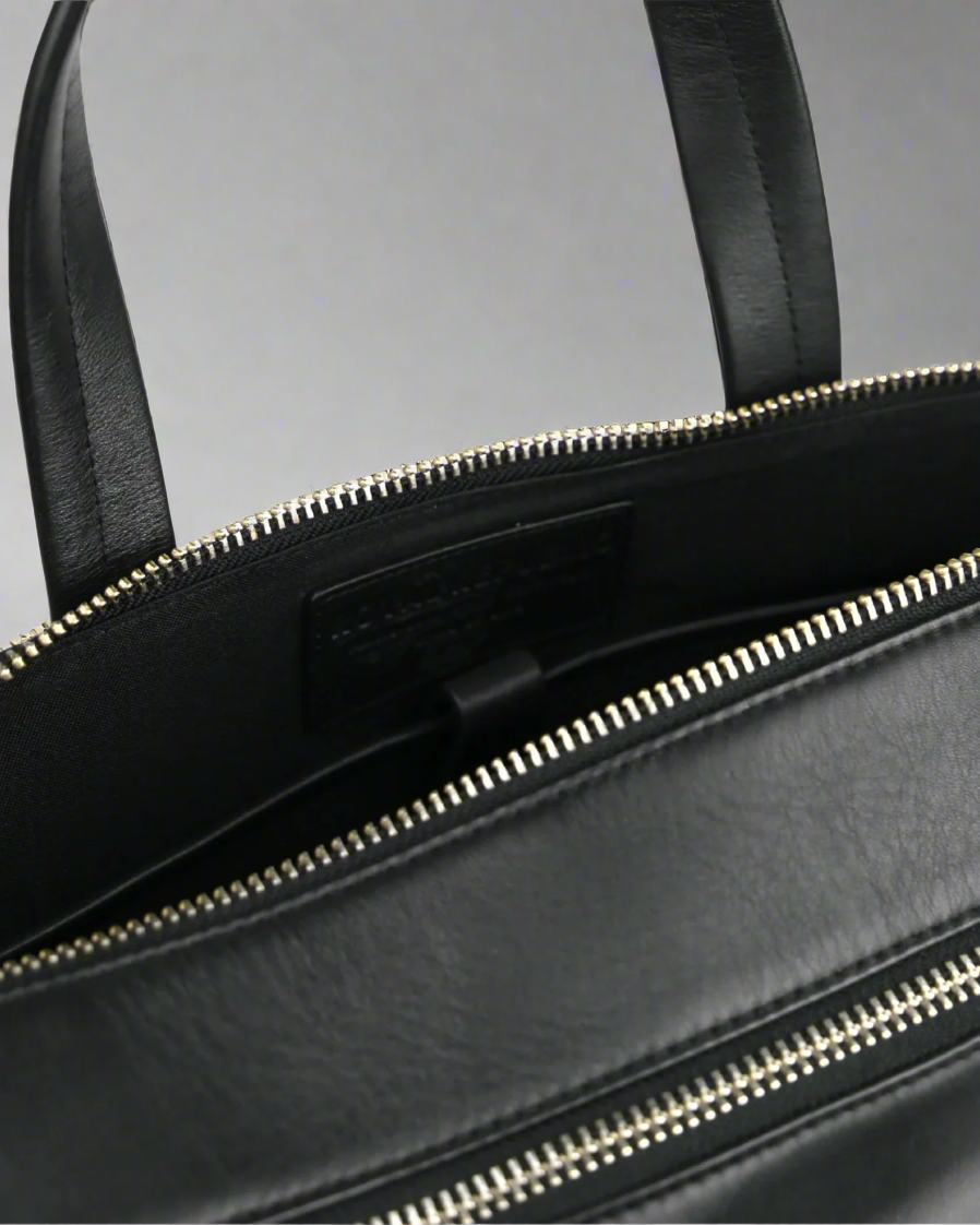 Close-up of a black Royal RepubliQ leather bag with silver zipper on a gray background