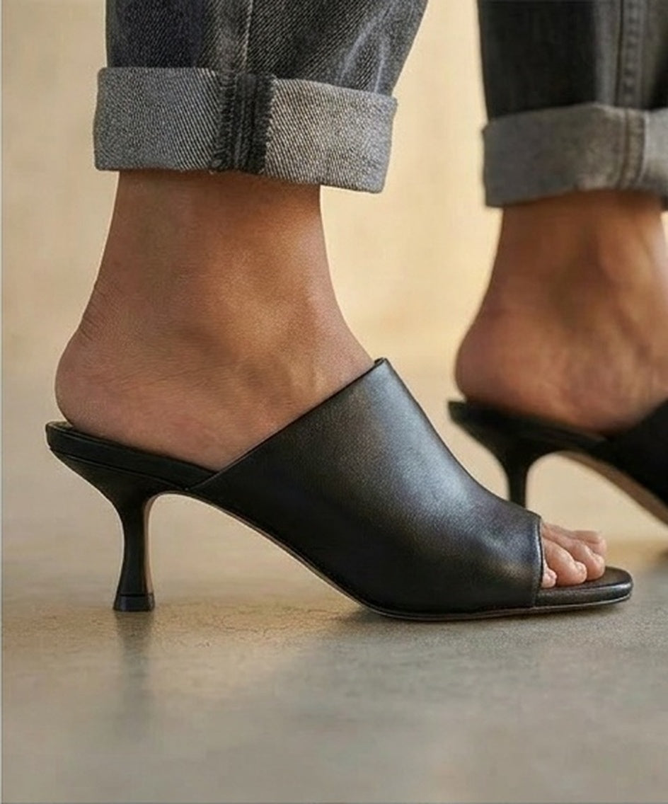Black open-toe kitten-heeled shoes worn with rolled-up jeans on a neutral background