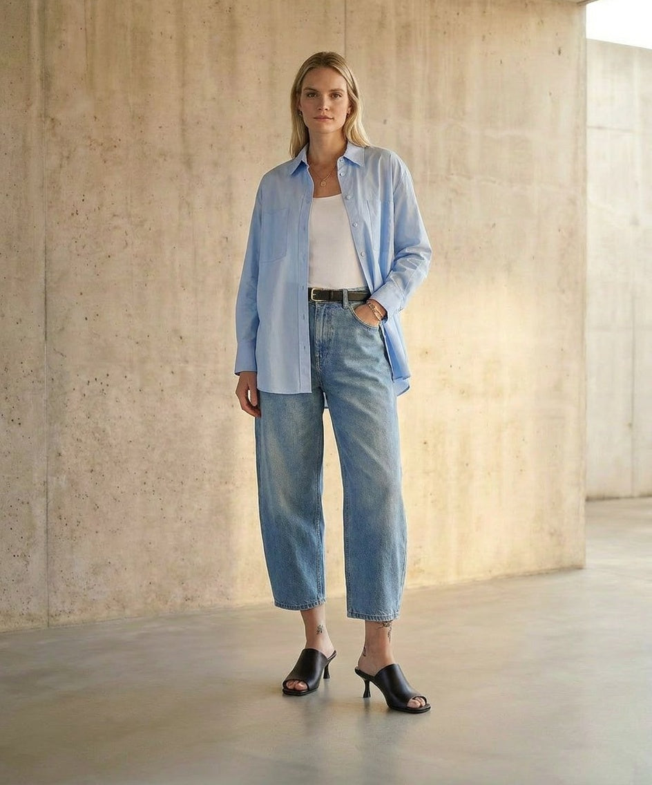 Woman wearing a light blue shirt and jeans standing against a concrete wall and wearing Atomic Mule Black