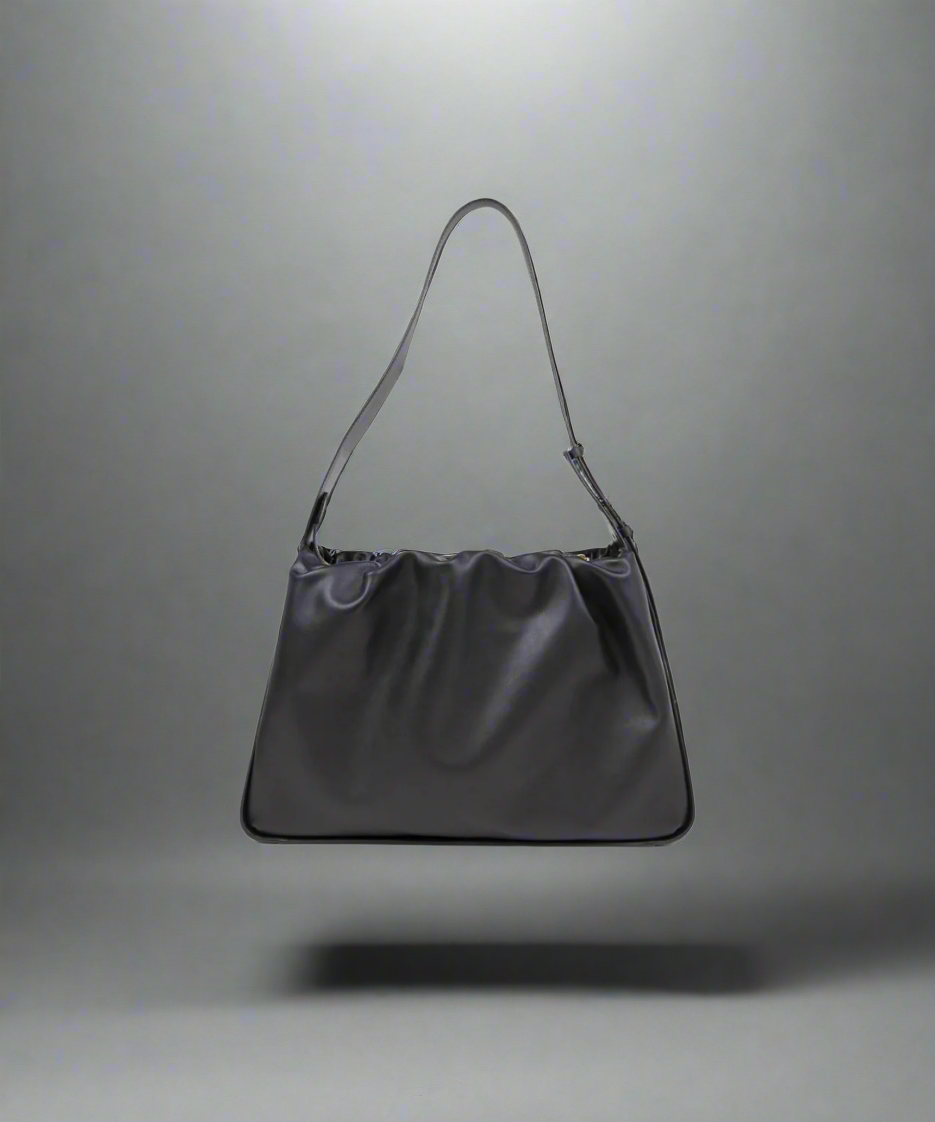 A black trapezoid handbag with a shoulder strap and gold trim, made from genuine cow leather.