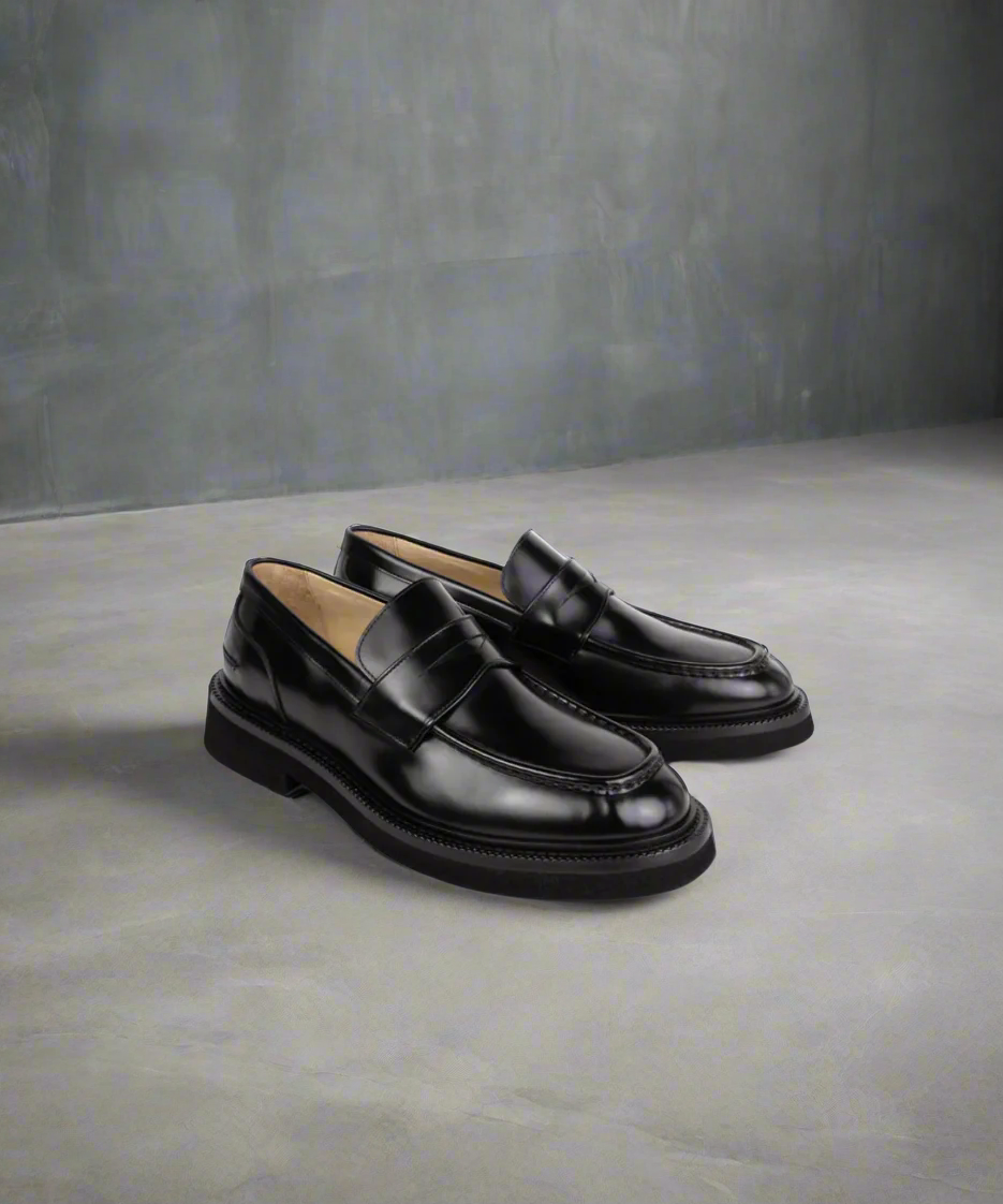 Pair of Royal RepubliQ black loafers on a gray surface with a neutral background