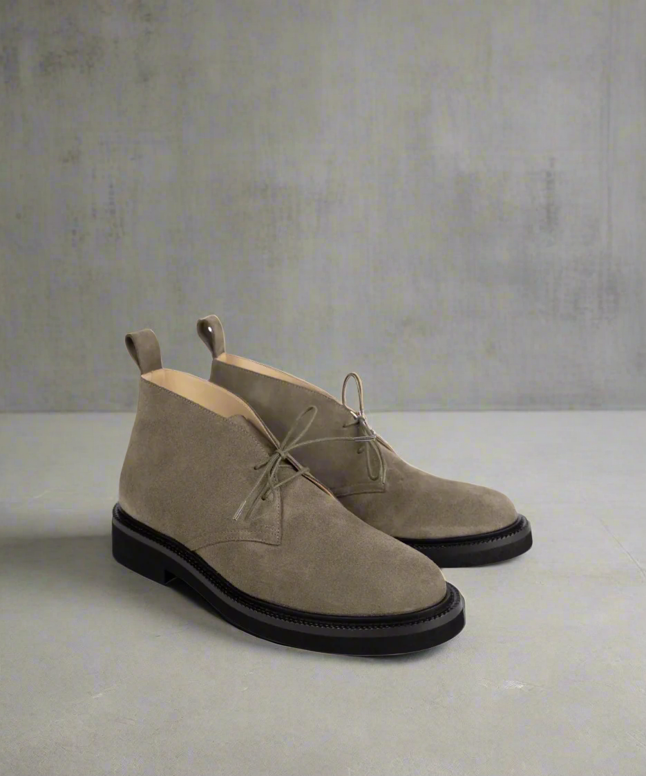 Pair of beige suede boots with black soles on a light gray background