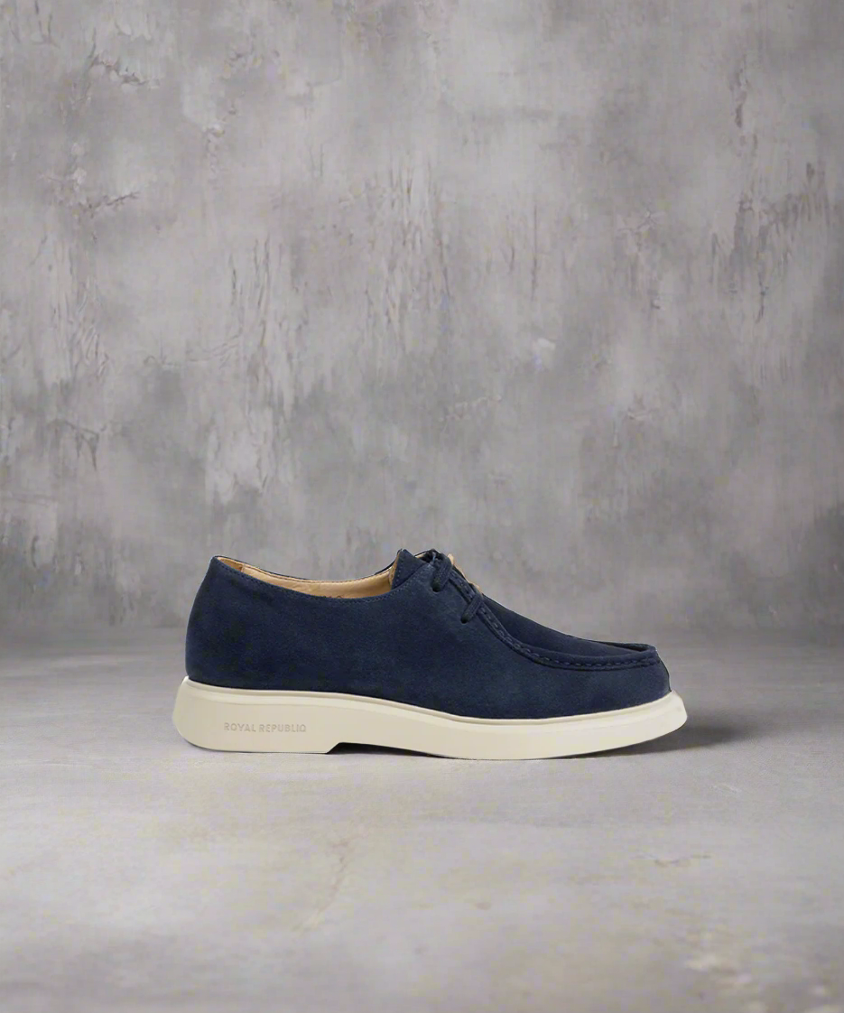 A navy blue Royal RepubliQ Suede Chukka boot with lace-up closure, showcasing the side profile against a gray background.