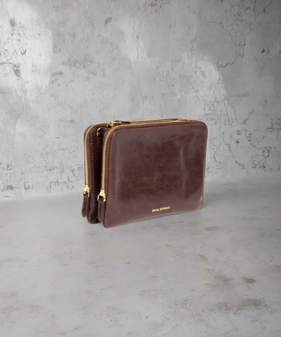 Brown Royal RepubliQ leather clutch bag with a strap on a gray background
