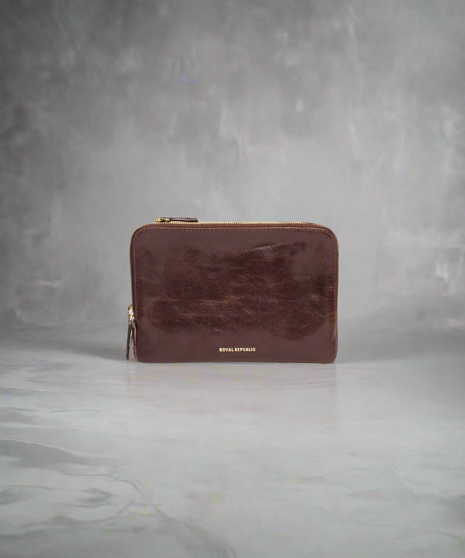 Brown Royal RepubliQ leather clutch bag with a strap on a gray background