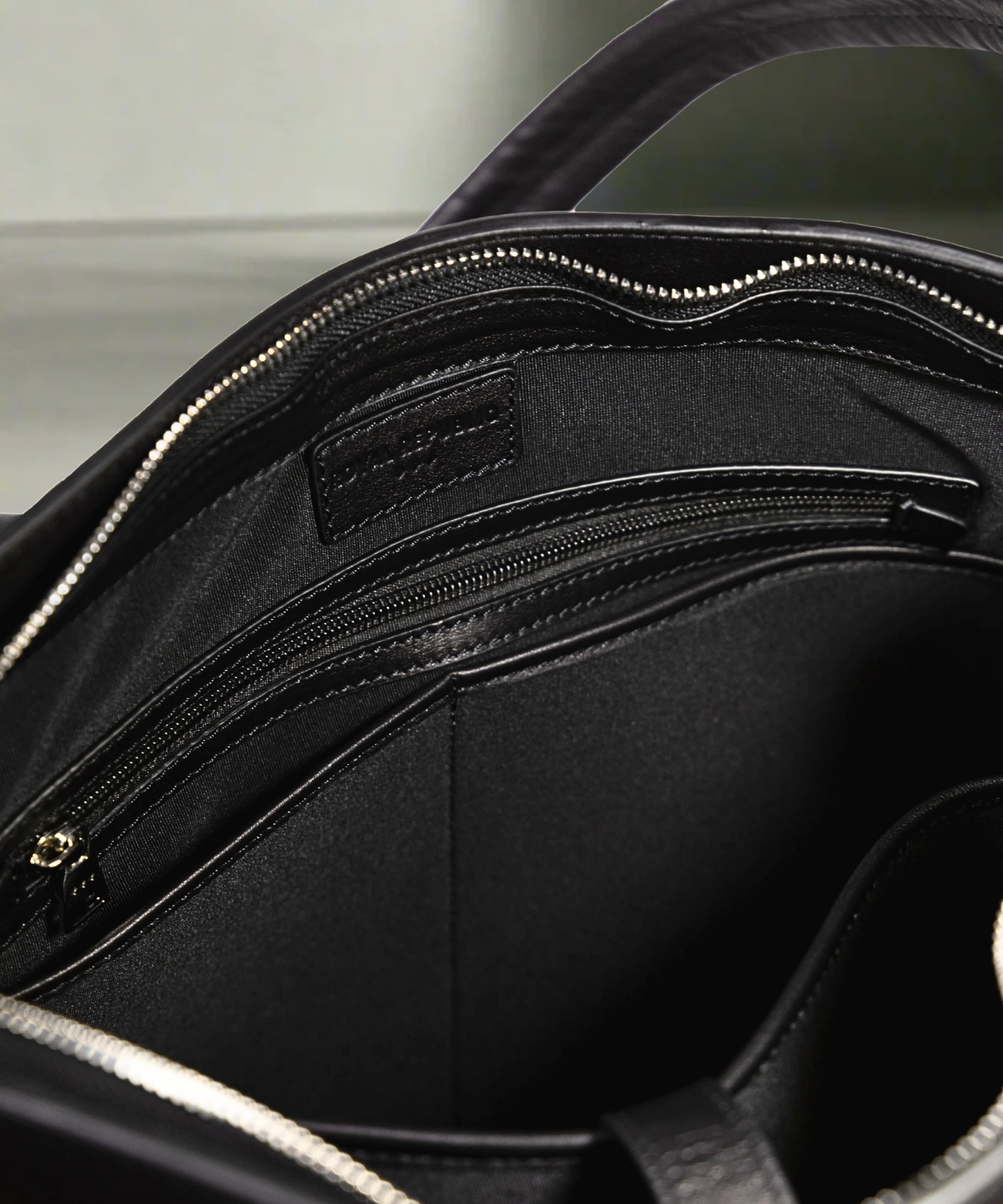 Inside view of a black Royal RepubliQ leather shopper bag with a shoulder strap and a handle, displayed against a plain background.