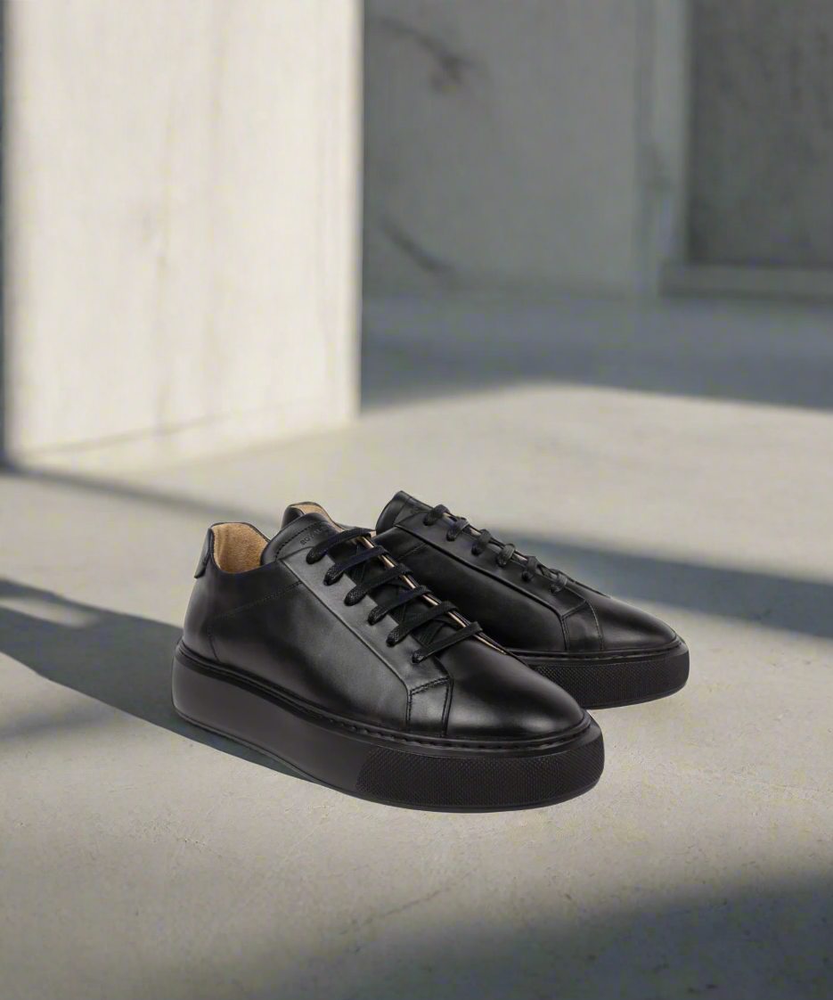 Pair of black Royal RepubliQ leather sneakers on a concrete surface with a neutral background