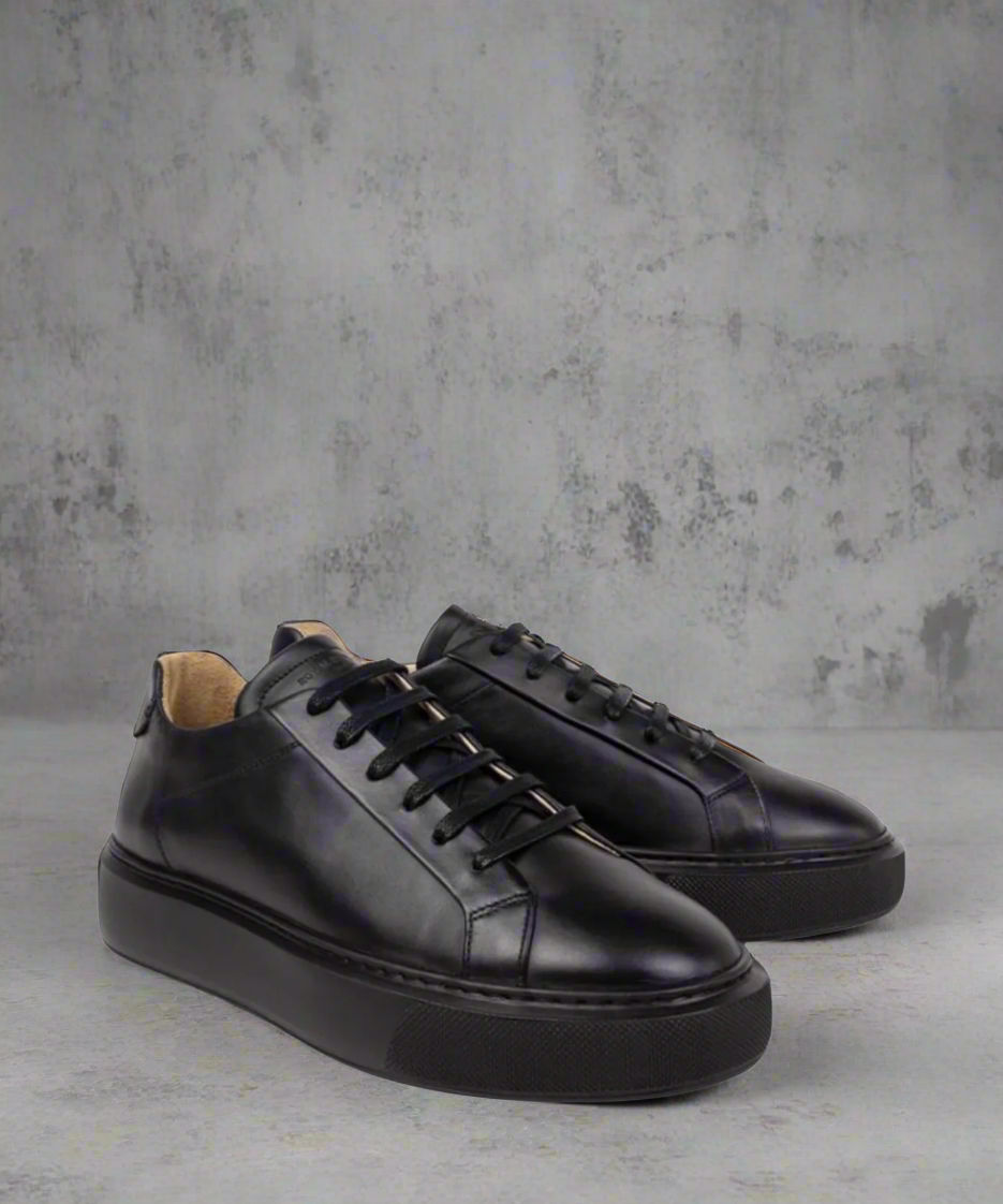 Pair of black Royal RepubliQ leather sneakers on a gray concrete background