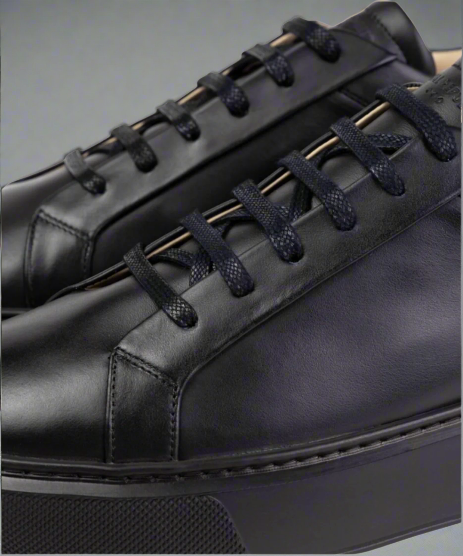 Close-up of a black Royal RepubliQ leather shoe with laces on a gray background