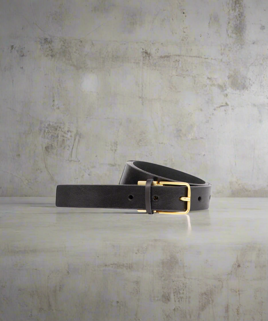Black Royal RepubliQ leather belt for women with matt gold buckle on a gray textured surface