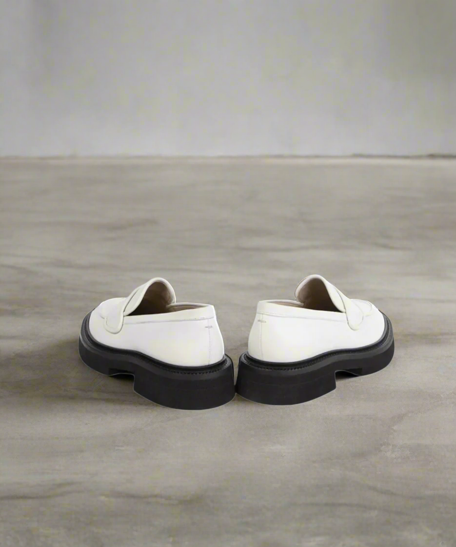 Pair of white loafers with black soles on a gray background