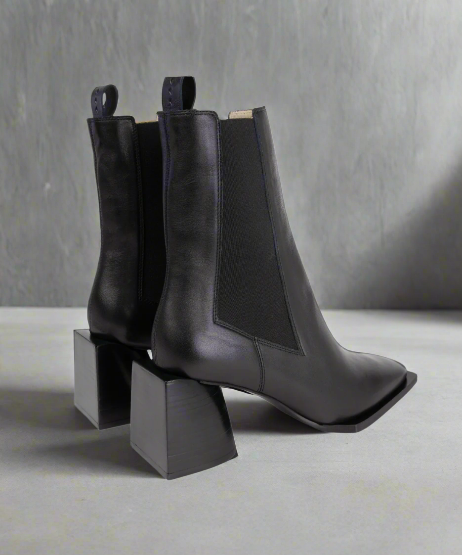 Black Royal RepubliQ leather ankle boots on a geometric black stand against a gray background