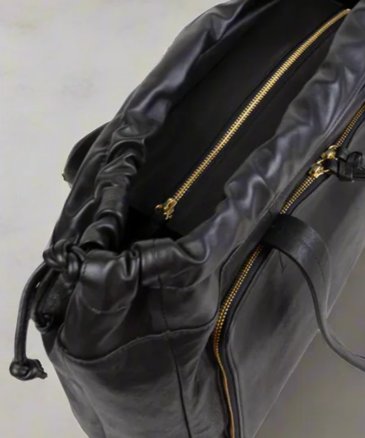 Close-up of a black leather bag with gold zipper details on a light gray background