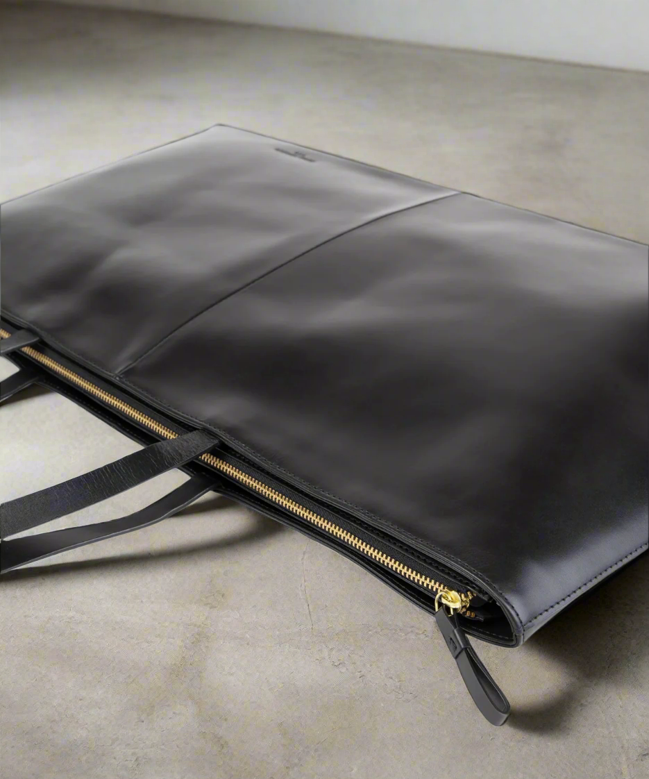 Black leather clutch bag with gold zipper on a gray background