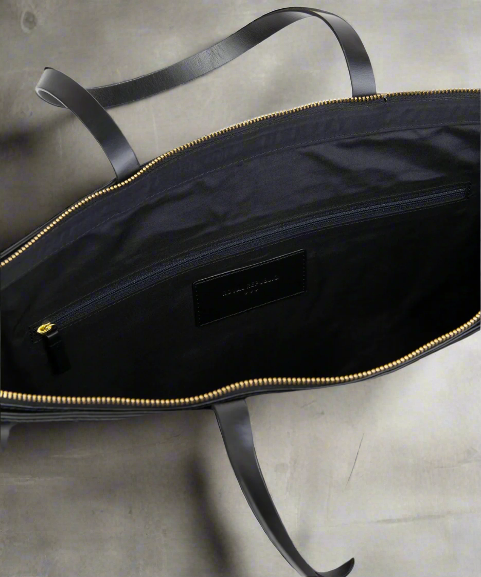 Black leather bag with gold zipper and visible brand label on a gray background