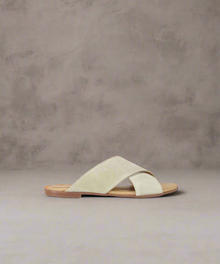 A beige suede cross sandal with a flat heel and padded leather strap.