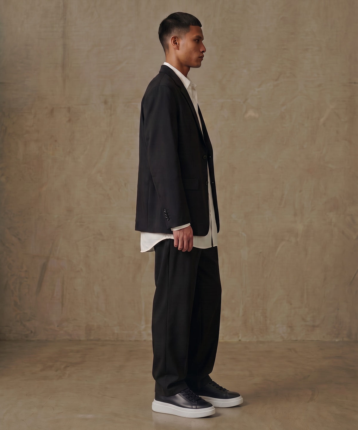 Model in black blazer wearing Vectra One black leather sneakers with white platform sole, side view