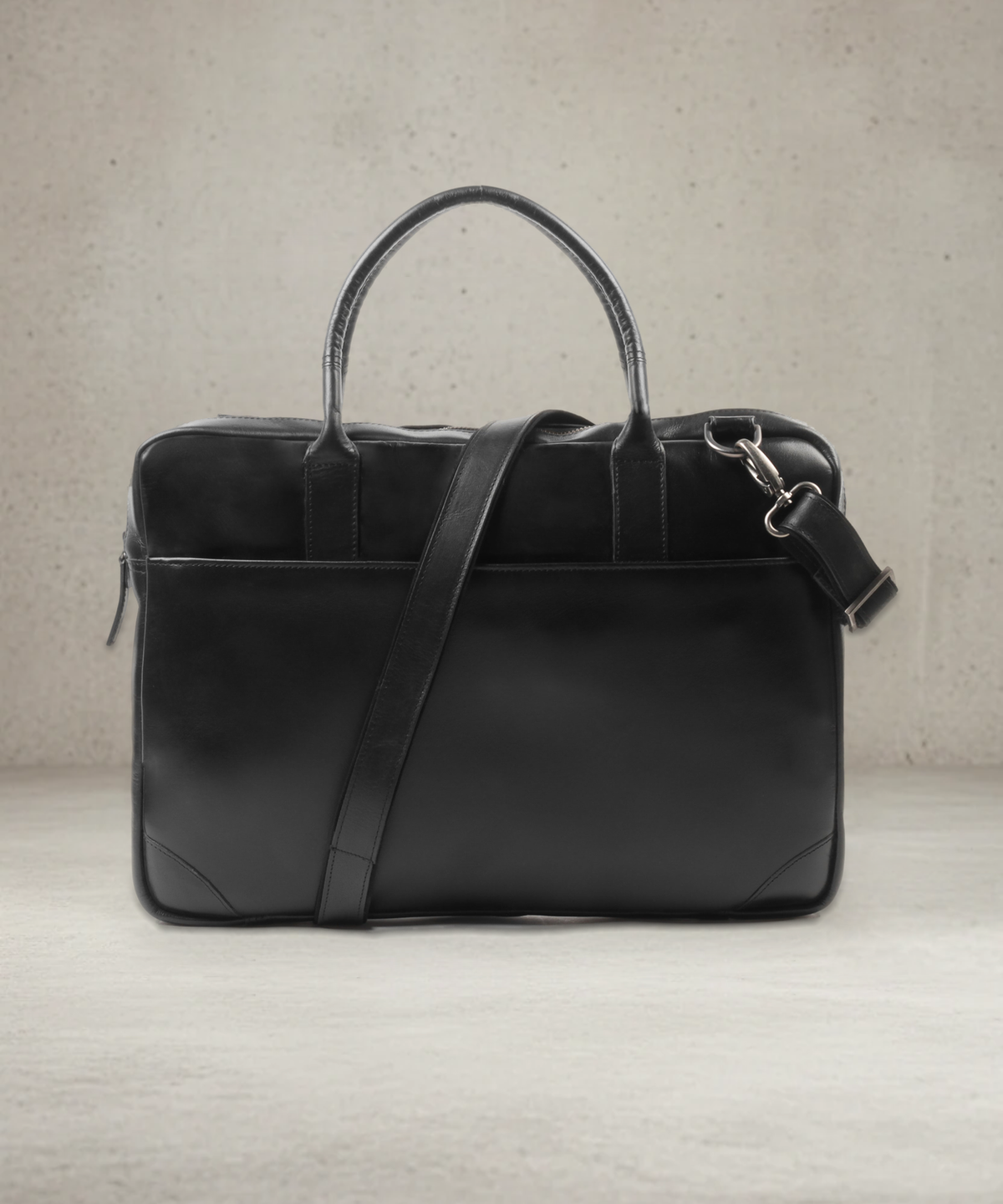 Black leather laptop bag with handles and detachable shoulder strap, front view on a concrete studio background